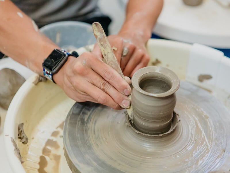 A person holds a small tool to a vase on a spinning pottery wheel